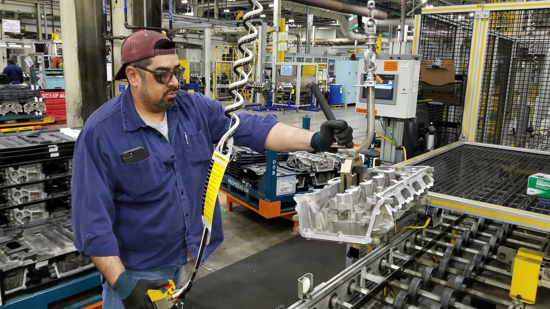 Worker uses tool to move engine parts into place on assembly line